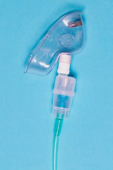 Coronavirus treatment concept. Close-up of a nebulizer mask or medical face mask for treatment of the respiratory tract over blue background. Macro photograph.