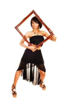 A gorgeous woman standing in the studio in a black dress looking trough.a picture frame, isolated for white background.
