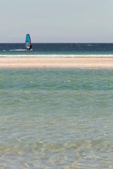 Windsurfer sailing near the sand of the beach with turquoise water in the foreground