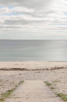 Board path to enter a beach without people and with a calm sea and cloudy sky