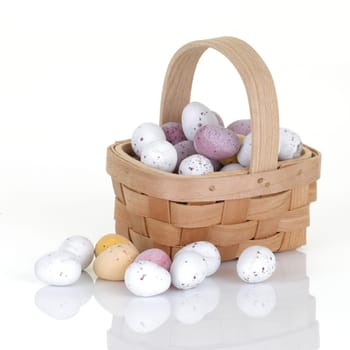 A wood basket of small easter egg candy on white with reflection