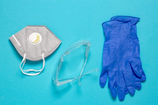 Coronavirus protective measures. Close-up of a N95 face mask or particle filtering half mask, a clear transparent safety glasses and medical gloves on blue background. Personal protective equipment.