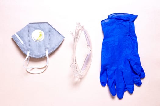 Coronavirus protective measures. Close-up of a N95 face mask or particle filtering half mask, a clear transparent safety glasses and medical gloves on a sparkling light pink paper background. Personal protective equipment.