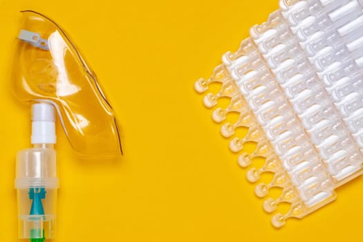 Coronavirus treatment concept. A medical face mask or nebulizer for treatment of the respiratory tract and several tens packs of ampoules flat layed on a yellow background. Copy space.