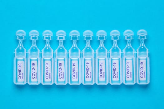 Coronavirus treatment concept. Close-up of ten ampoules with vaccine COVID-19 flat layed on a blue background. Global pandemic outbreak and healing the deadly coronavirus. Macro photograph.