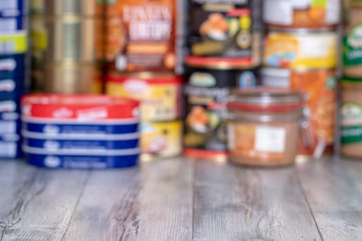 Coronavirus outbreak. Blurred image of stack of canned foods with a long shelf life such as fish, vegetables and meat stew, sausages and other goods on a table. Purchases in fear of coronavirus.