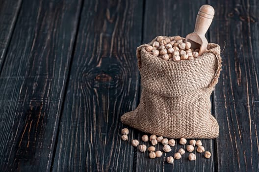 Sack with chickpeas and spoon stands on wooden background