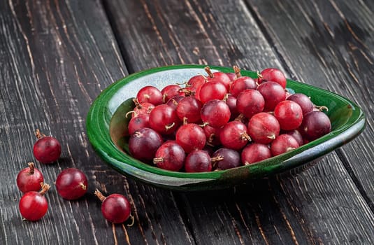 Red gooseberries on a dark table in a clay bowl