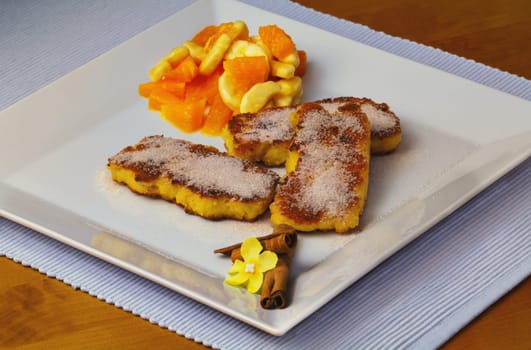 Baked semolina slices with fruit salad appetizingly arranged with cinnamon sticks and blossom as decoration.