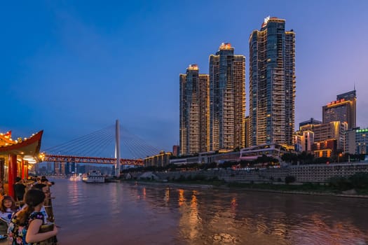Chongqing, China -  August 2019 : Passengers on the viewing deck of the city sightseeing boat admiring the night view of the modern commercial and business buildings on the riverside at dusk