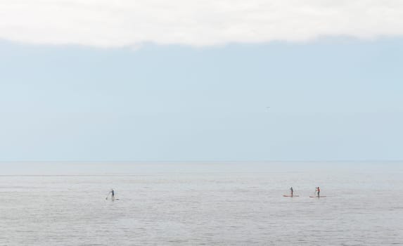 Three people practice paddle surfing in a totally calm sea