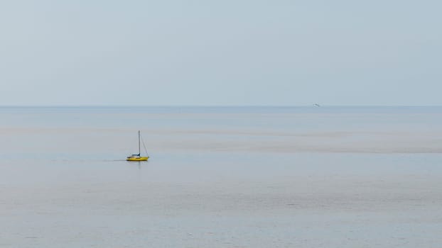 Yellow boat with its sails gathered up and stopped in a totally calm sea