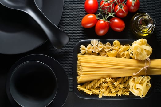 Raw pasta collection and tomatoes on black table