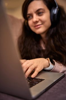 woman in headphones using laptop and lying on sofa at home