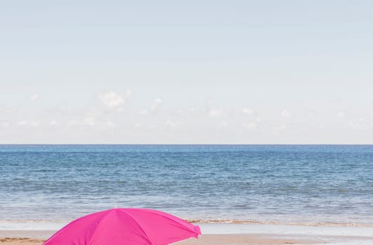 Magenta umbrella in the foreground on a lonely beach with a calm sea