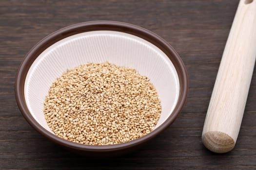 White sesame seeds in a mortar with wooden pestle on table