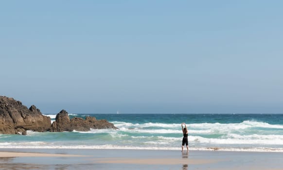 Blonde girl stretching her back as she watches the waves on the seashore