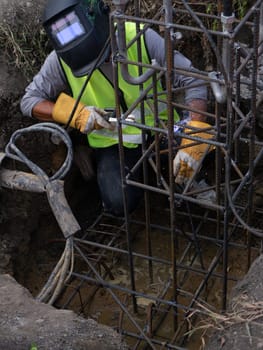 Worker in protective mask welding steel railings outdoors, sparks fly down