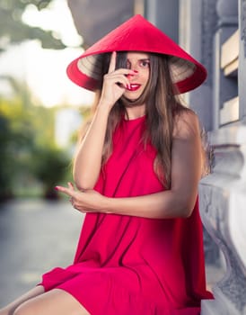 Fashion portrait of a beautiful woman in red conical hat outdoor