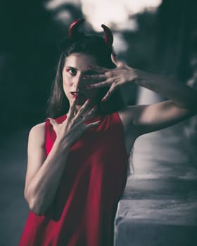 Fashion portrait of a beautiful woman in red dress and horns. Halloween