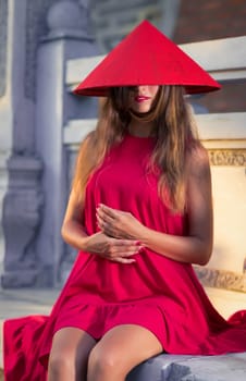 Fashion portrait of a beautiful woman in red conical hat outdoor