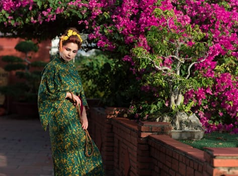 Fine art portrait of beautiful woman in Japanese Geisha style wearing kimono in a garden