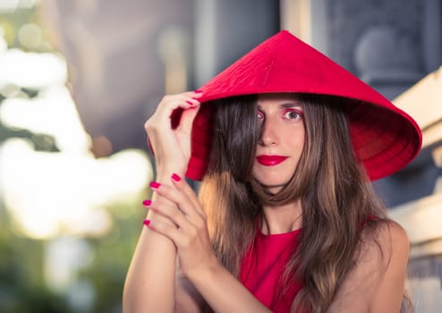 Fashion portrait of a beautiful woman in red conical hat outdoor