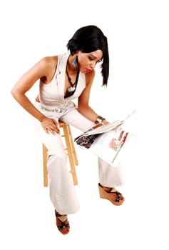 A gorgeous young woman in a white outfit sitting on a chair reading.her paper, isolated for white background.