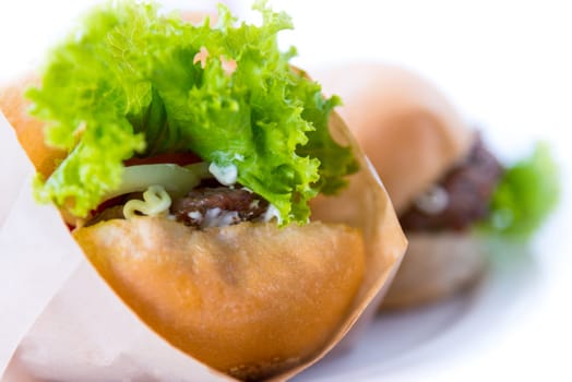 Burger is delicious American fast food, Closeup a hamburger made from pork or beef, green lettuce bread onion and tomato in a paper bag on a white table background at home to picnic or party