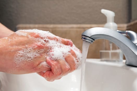 Washing hands with soap and water in bathroom sink, protection against viruses and bacteria, hygiene to stay healthy