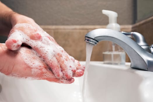 Washing hands with soap and water in bathroom sink, protection against viruses and bacteria, hygiene to stay healthy