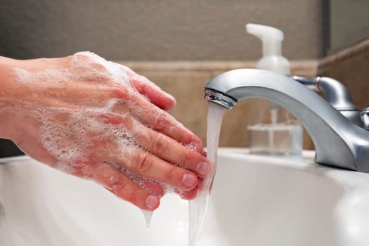 Washing hands with soap and water in bathroom sink, protection against viruses and bacteria, hygiene to stay healthy