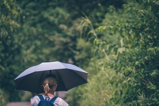 A view of a blond woman holding an umbrella while walking in a tree-covered field