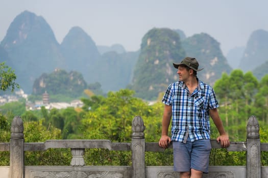 A view of a male laying on the fence and enjoying the beautiful view of the karst mountains in Yangshuo in the morning