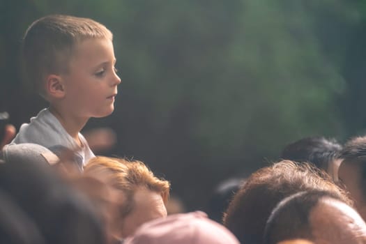 A beautiful close up of a little boy sitting on his father's shoulders surrounded by people