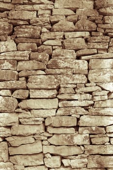 A vertical greyscale shot of an old wall made with uneven sizes of rocks