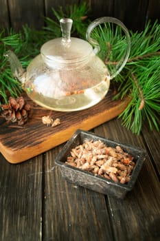 Tea pot of herbal tea with pine buds on wooden background, vertical image