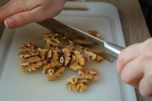 Female hand is cutting walnuts with a kitchen knife