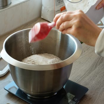 Hand is putting flour into a bowl for baking