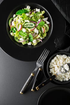 Healthy Green salad with fresh vegetables and fresh cheese on black background close up