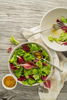 Healthy red and green lettuce salad meal on wooden table background. Eating fresh radicchio and young lettuce with dressing sauce