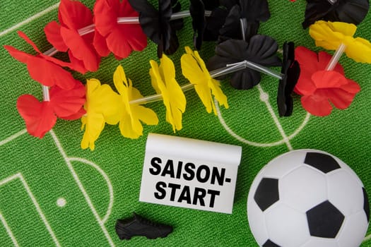 Saison Start in german language means season beginning. Soccer Ball with flower necklace in the colors of german flag and calendar