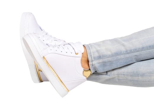 Women legs in jeans and sneakers. Woman legs in light denim pants wearing modern white sneaker. Fashionable white footwear. Macro photograph.