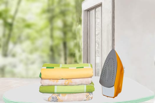 Household laundry ironing. Close-up of a yellow electrical iron and a stack of ironed clothes on an ironing board indoors over blurred green natural background. Advertising for the laundry service with space.