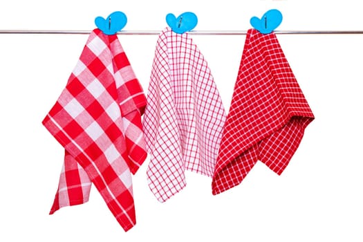 Hanging towels isolated. Closeup of various red checkered kitchen towels with blue clothespins hang on a clothes rail isolated on a white background.