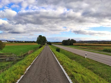 country road through rural landscape with blue sky and clouds