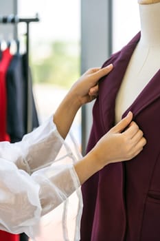 Close-up young adult asian fashion designer checking at suit arm on mannequin at her atelier studio as before deliver to her customer. For entrepreneur small business startup work from home concept.