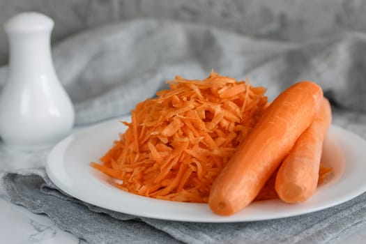 Grated carrots on a white plate and two whole carrots nearby