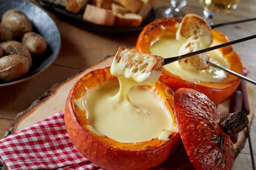 Serving of melted cheese fondue in a restaurant served in a roasted hollowed out pumpkin with toasted baguette and potatoes for dipping and a glass of wine