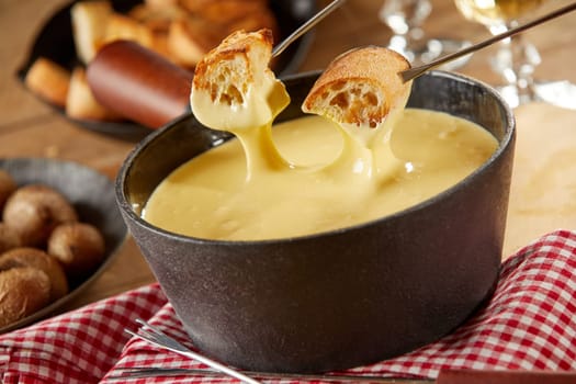 Traditional Swiss cheese fondue in cast iron pot in close up on a rustic table with side dishes showing forks with toasted bread being dipped